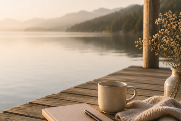 A peaceful lakeside scene at sunrise with a wooden dock, a notebook, a warm drink and a blanket, symbolising rest, reflection and recovery.